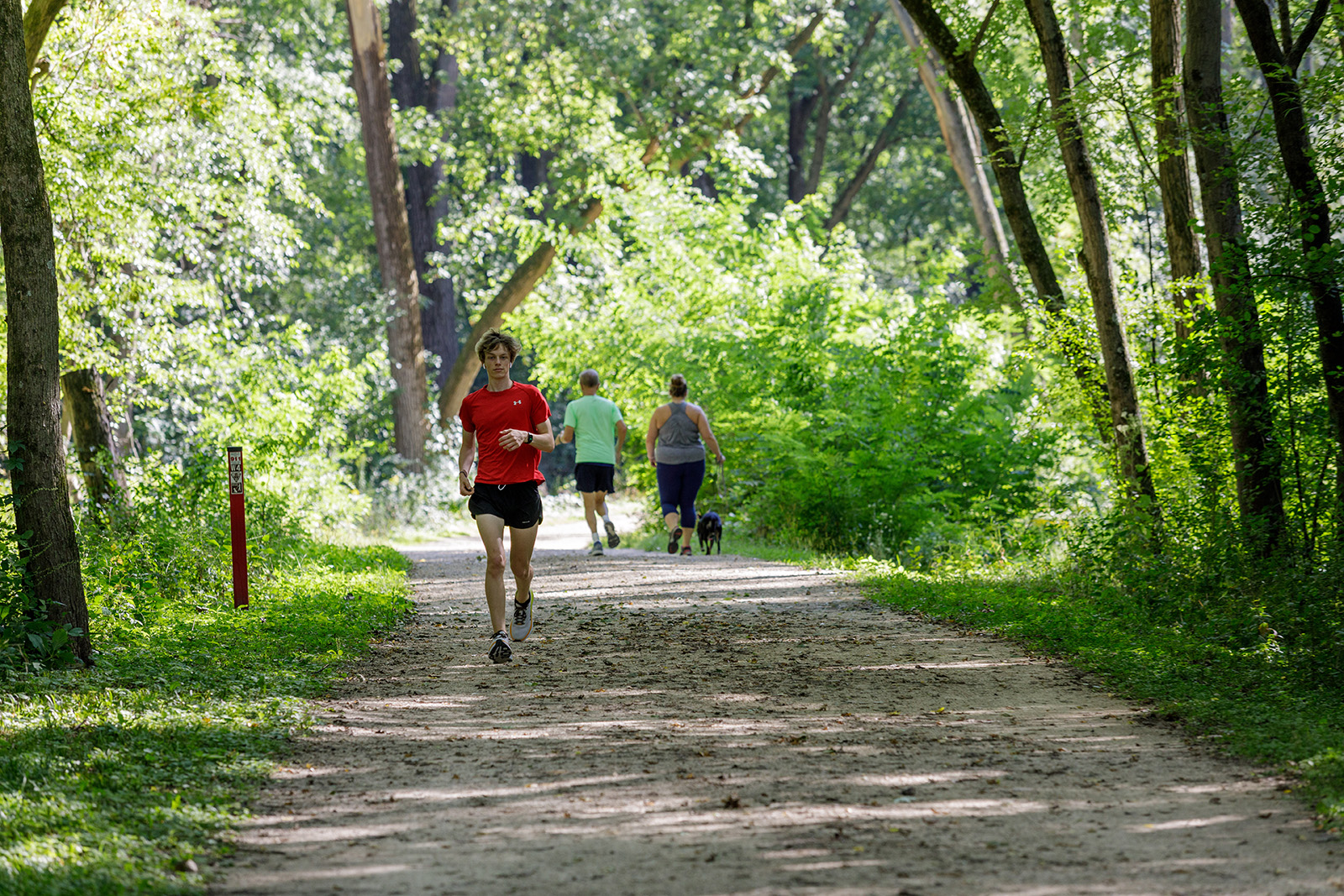a woman running down a dirt road in the woods.
