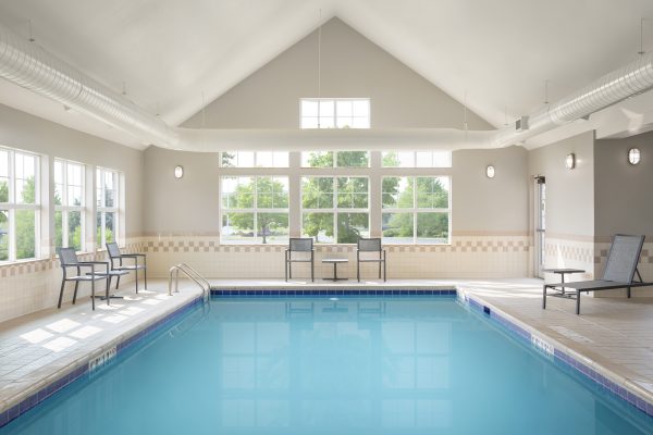 An indoor swimming pool with lounge chairs and windows.
